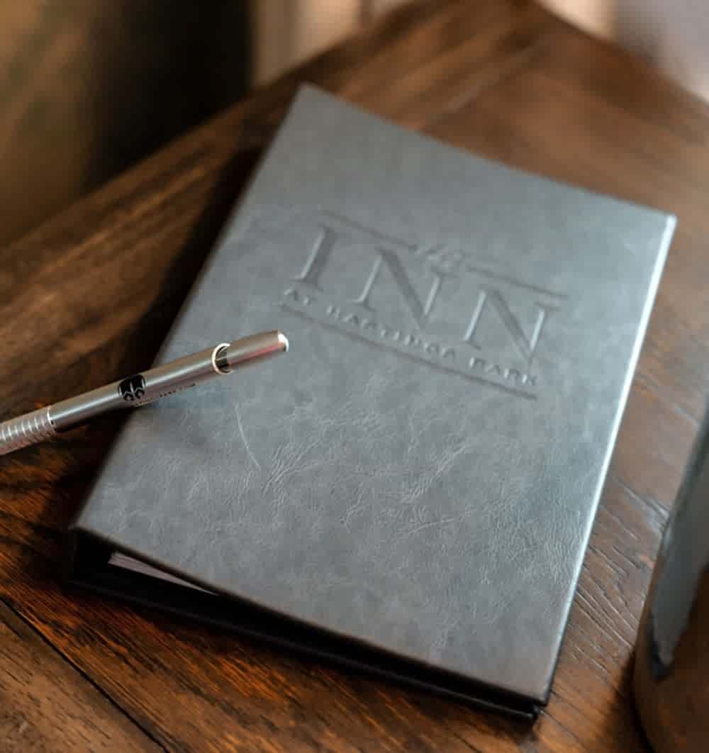 A silver pen rests on a gray folder embossed with The Inn at Hastings Park, placed on a wooden table.