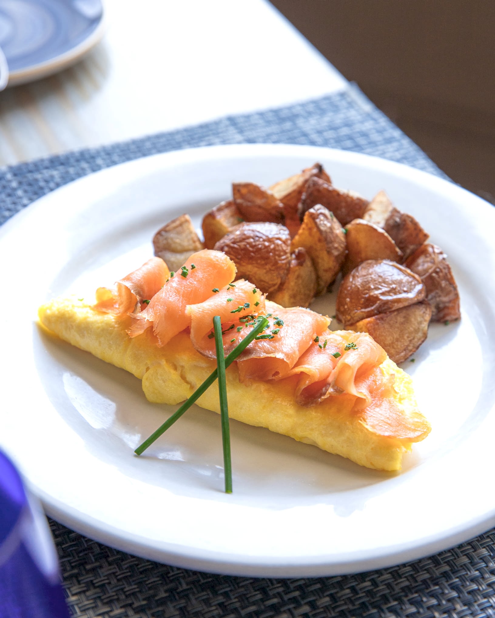 Omelet topped with smoked salmon and chives, served with roasted potatoes on a white plate.