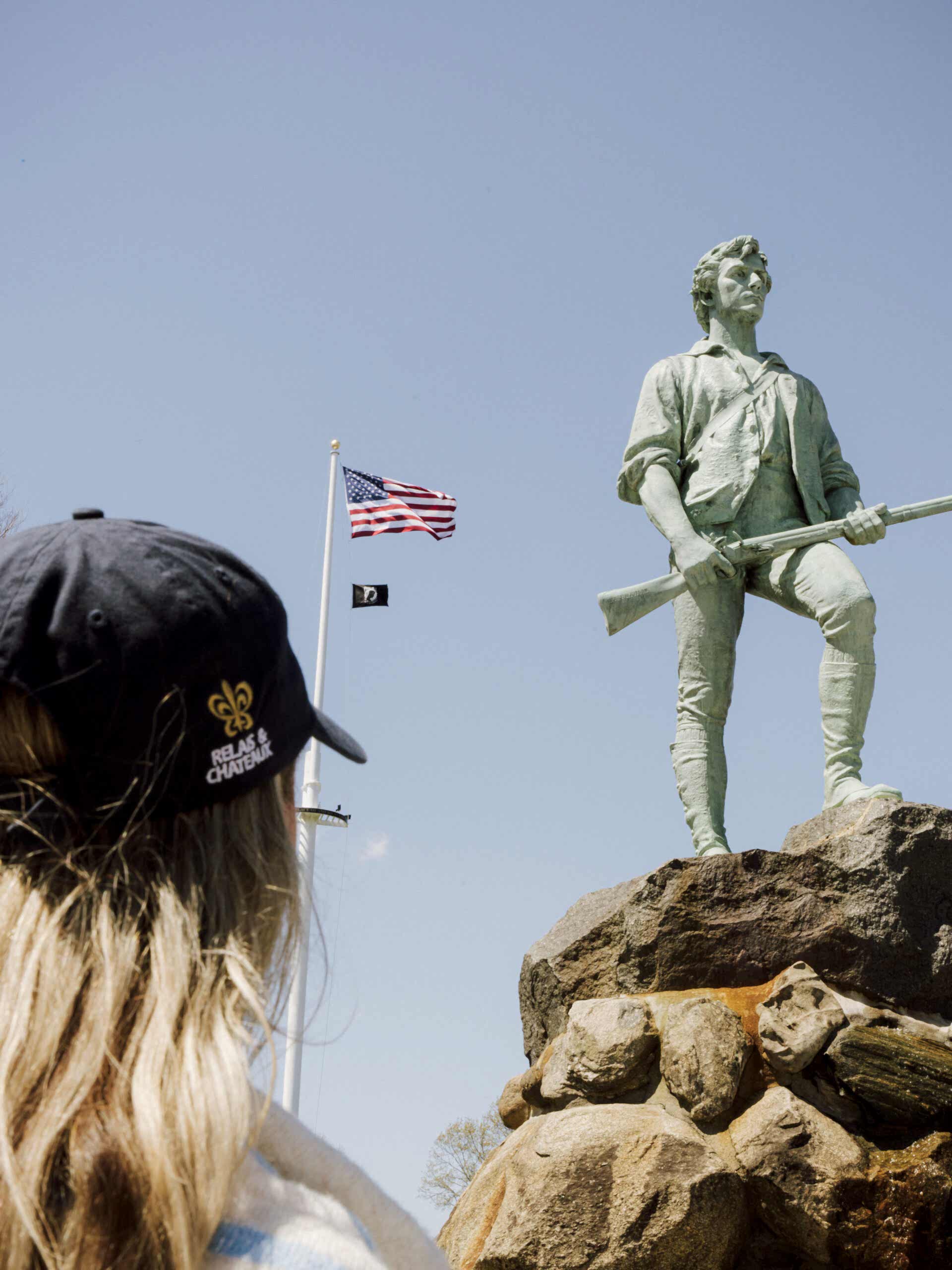 Woman staring at a minuteman statue with a usa flag