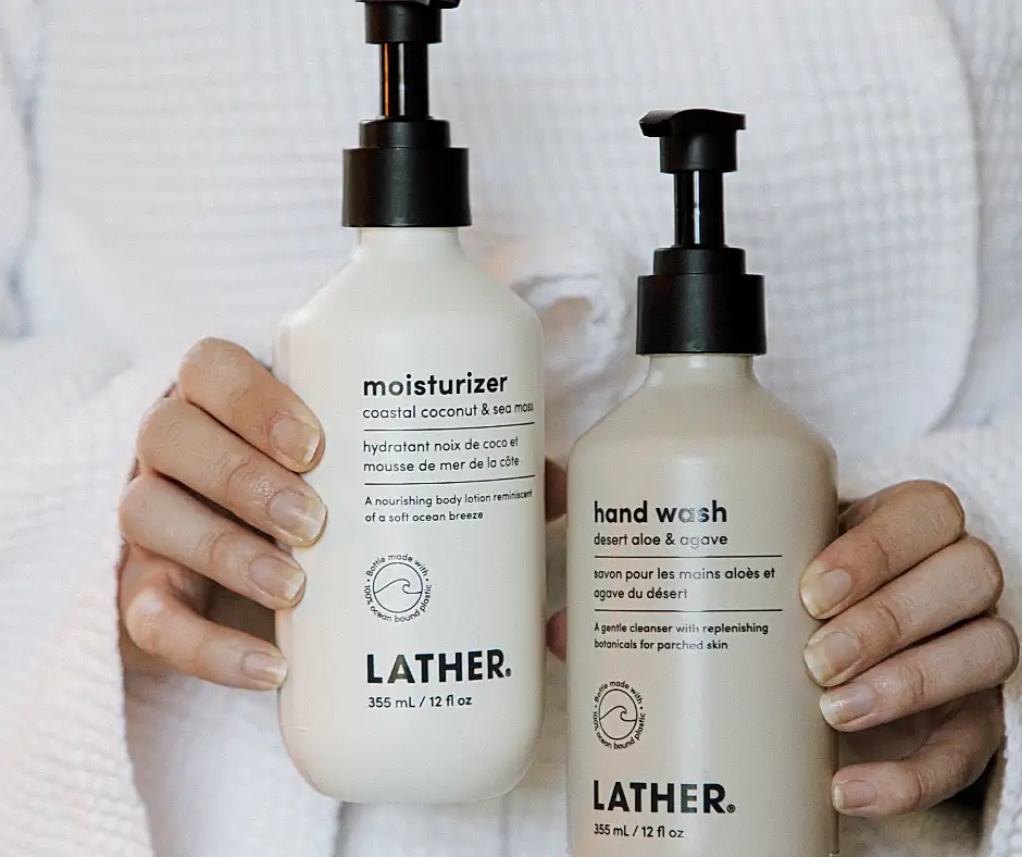 Person in a white robe holding two LATHER brand bottles: moisturizer (coastal coconut) and hand wash (desert aloe & agave).