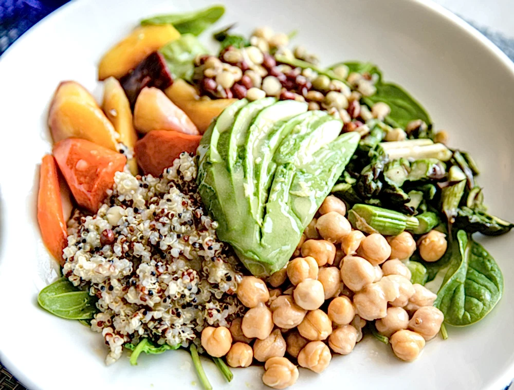 A colorful salad bowl with sliced avocado, chickpeas, quinoa, leafy greens, tomatoes, and assorted vegetables arranged neatly on a white plate.
